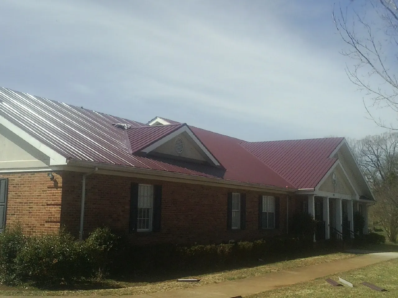 Red metal roof with gabled entries on a long brick building, from a Hail Damage Roof Repair job in Grand Rapids