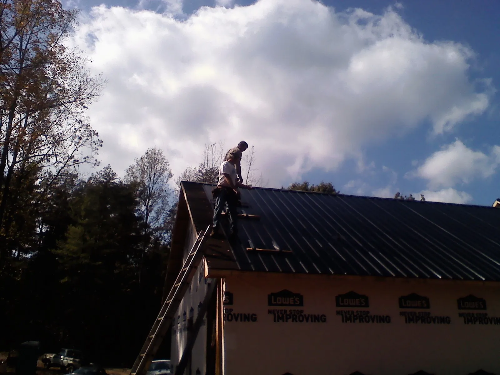 Roofer fastening dark metal panels high against a cloudy sky, from a Roof Inspection job in Grand Rapids