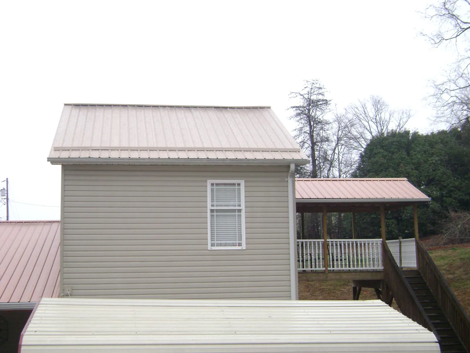 Tan metal roofs on a two story addition and attached porch, from a Roof Replacement job in Grand Rapids